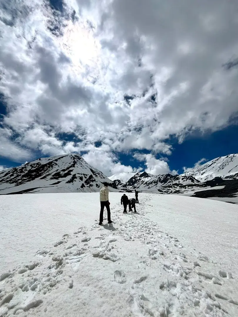 Two figures crossing a snowfield below snow-capped peaks, Himachal Pradesh. Photograph by Arav Jain.