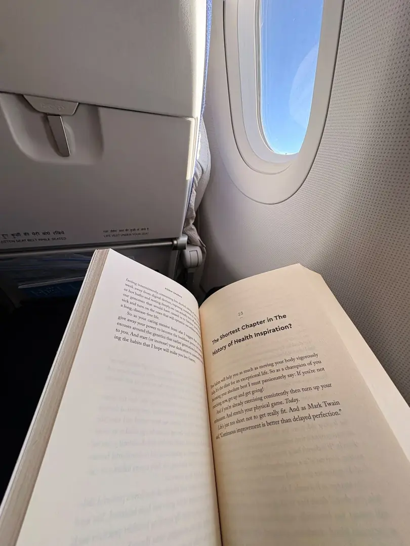 An open book on a tray table beside an aircraft window. Photograph by Arav Jain.