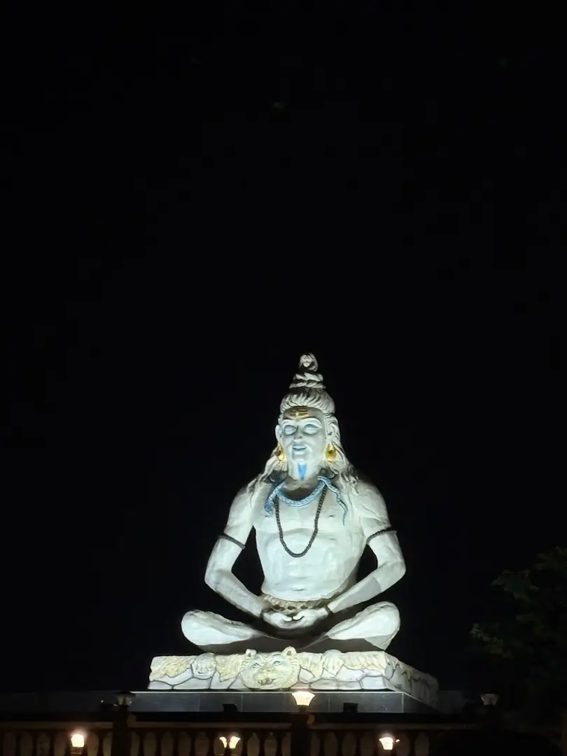 An illuminated Shiva statue seated against a black night sky. Photograph by Arav Jain.